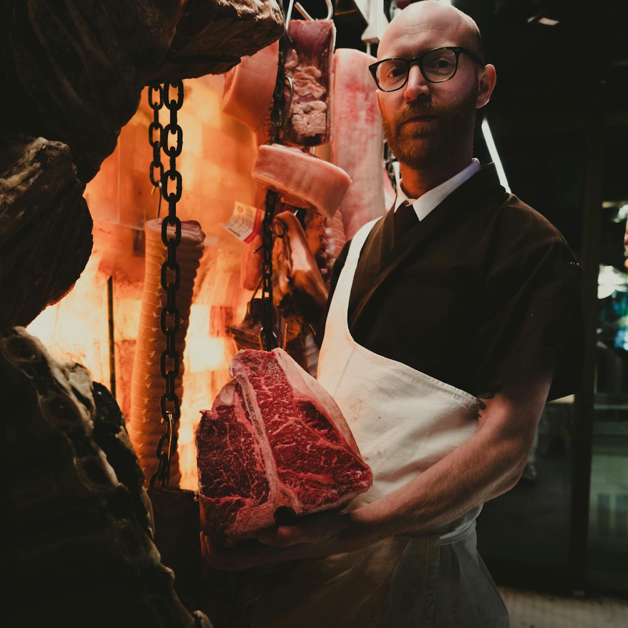 Butcher holding a large cut of meat in a meat display, surrounded by various meat products, reflecting livestock meat production tracking.